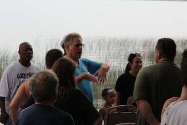 A group of people gathered outdoors near tall grass, engaging in conversation.