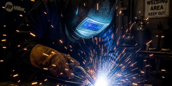 Welder in protective gear creating bright sparks during welding.