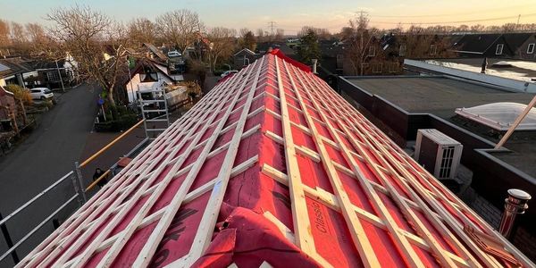 Roof construction with wooden battens on red underlayment during sunset.