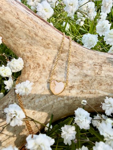Gold heart-shaped necklace on natural antler surrounded by white flowers.