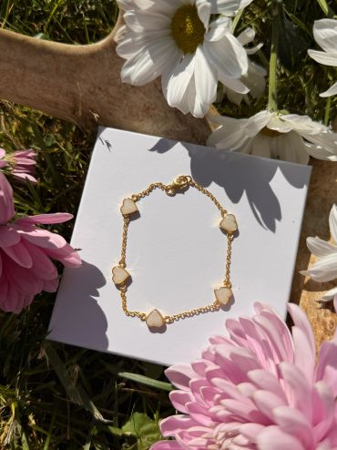 Delicate gold bracelet with heart-shaped stones displayed on a white card surrounded by flowers.