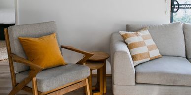 Cozy living room with a wooden armchair and gray sofa accented by warm-colored pillows.