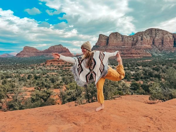 Woman practicing yoga on a rock with red mountains in the background.