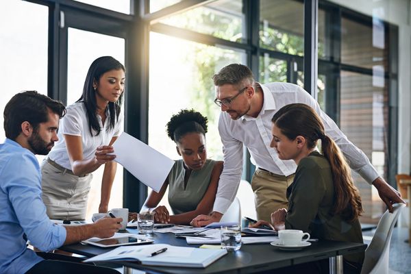 Five professionals of varying apparent ethnicities collaborate around a table in a bright office.