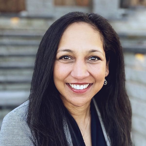 Smiling woman with long black hair wearing a checkered blazer.