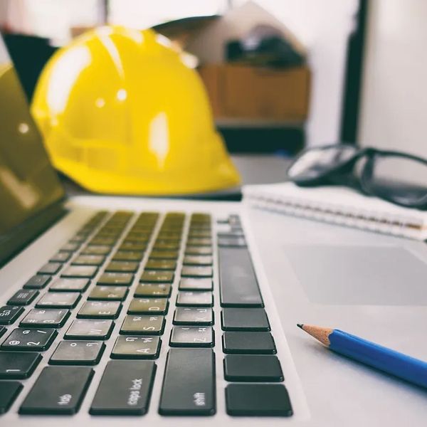 Close-up of a laptop keyboard with a yellow safety helmet and a pencil in the background.