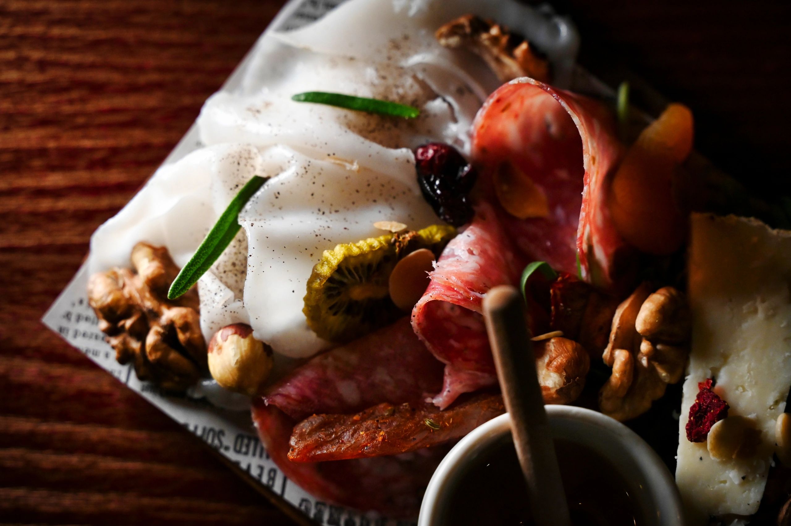 Close-up of a charcuterie plate with meats, cheese, nuts, and herbs.