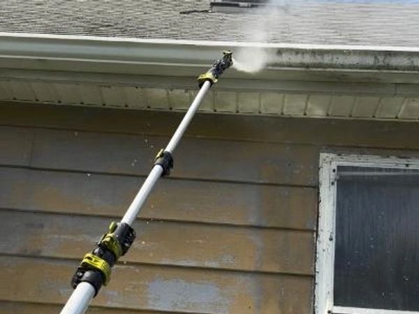 A pressure washer cleaning the exterior gutter of a house.