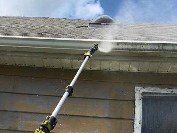 A pressure washer cleaning the exterior gutter of a house.