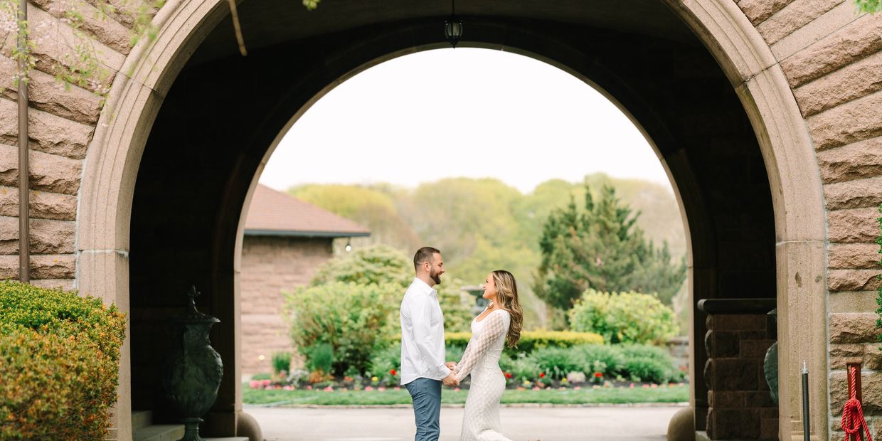 Couple holding hands under a stone arch surrounded by greenery.