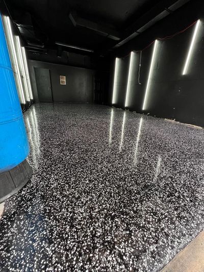 A glossy black floor with white and silver speckles reflecting the bright white lights 