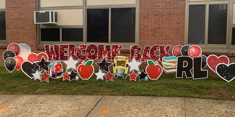 Colorful welcome back sign with school-themed decorations outside a building.