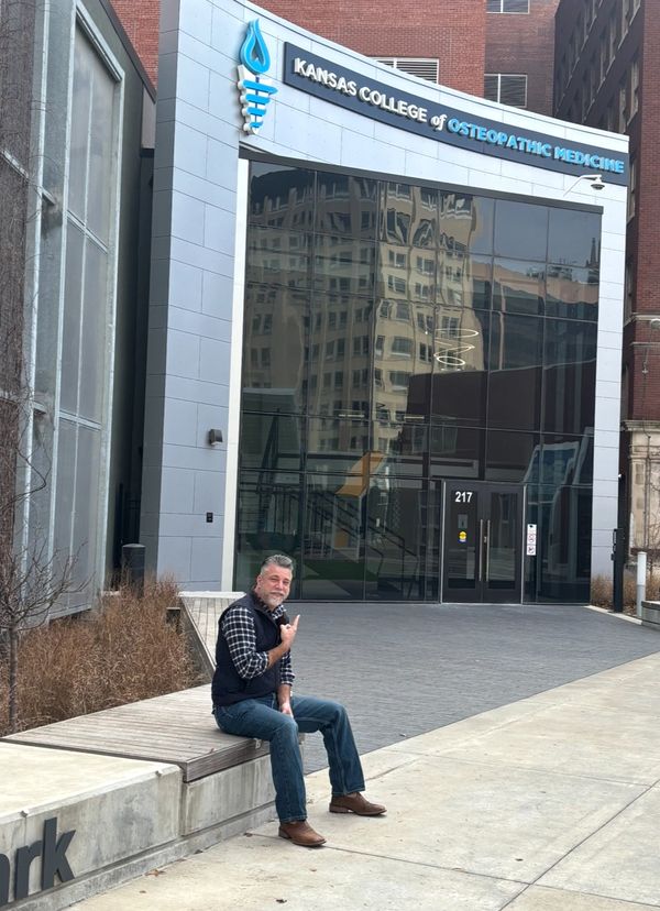 Aaron Kreag seated outside the main entrance of the Kansas College of Osteopathic Medicine