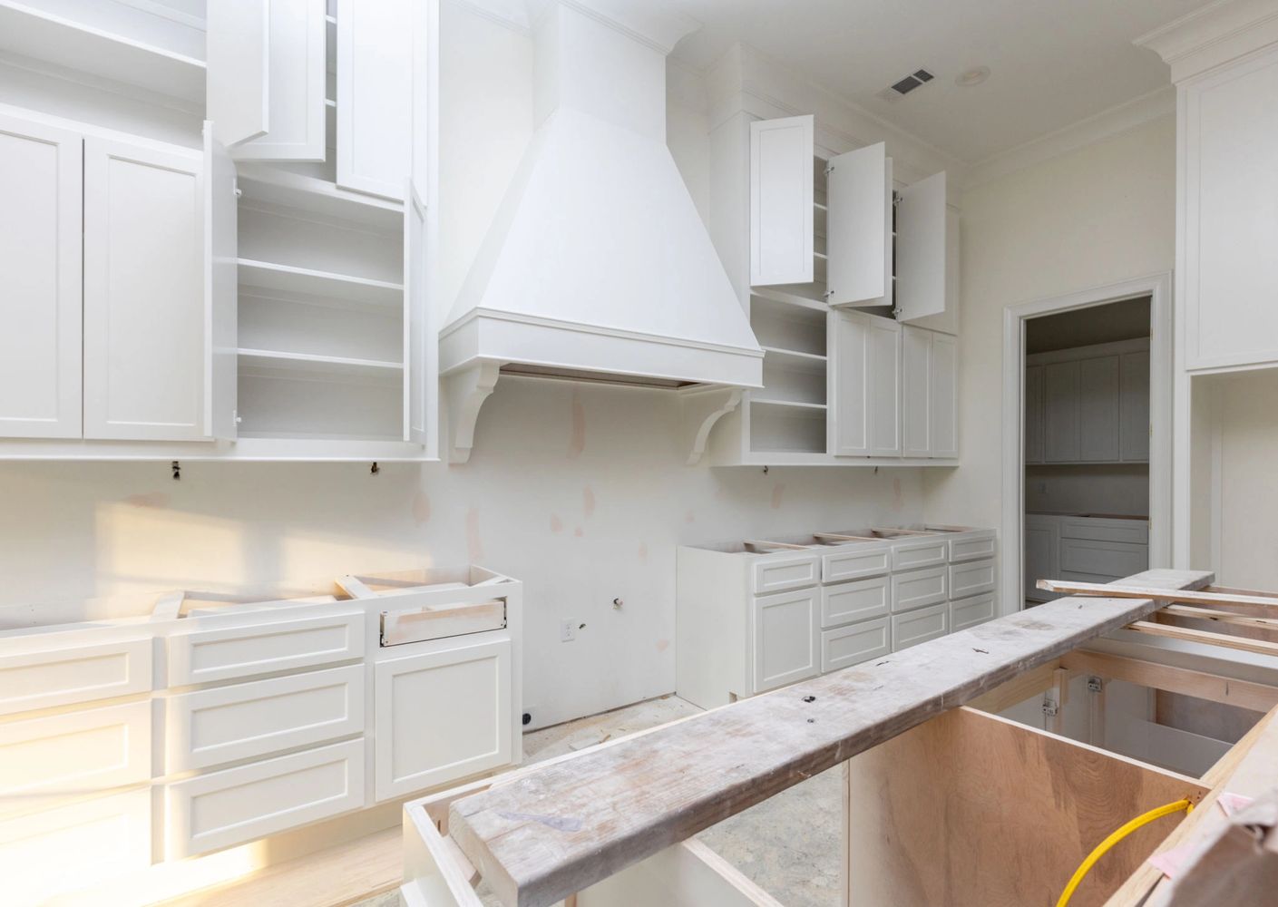 A white kitchen under renovation with open cabinets and no countertops. Cabinet painting