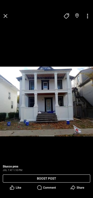 Two-story house with fresh white stucco and black window trims under renovation.