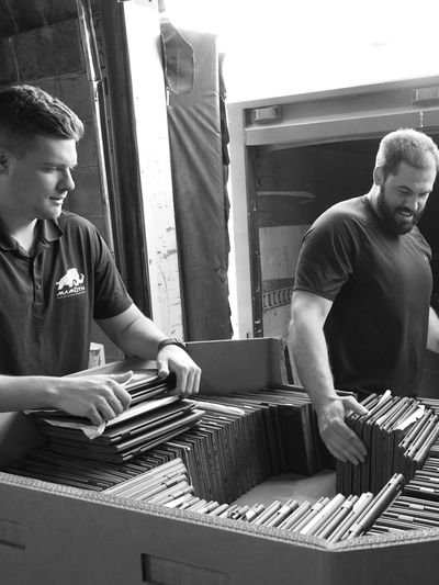 Two men sorting and handling laptops in a large cardboard box.