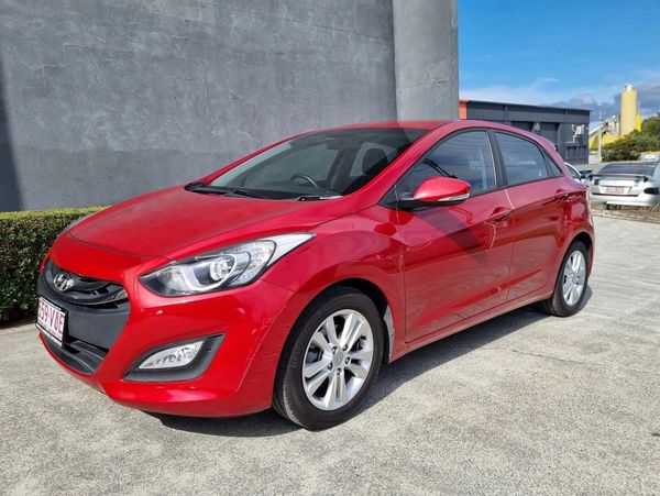 Red Hyundai hatchback parked outdoors on a sunny day.