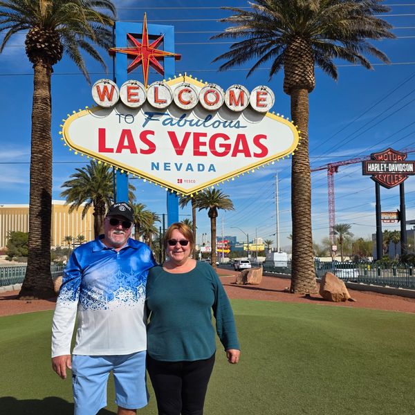 Visitors posing at the iconic “Welcome to Fabulous Las Vegas” sign on a sunny day