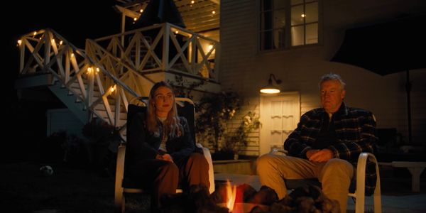 an elderly man and woman sitting on a chair, looking out into the fire