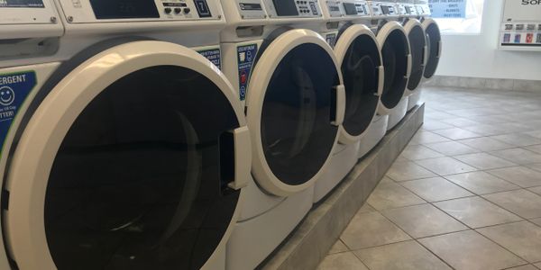 A row of industrial front-loading washing machines in a laundromat.