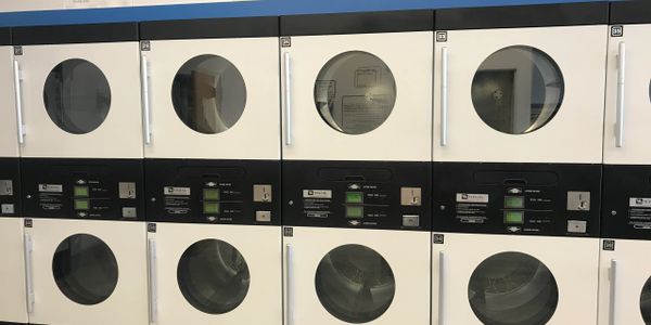 Row of white and black Maytag dryers in a laundry room.