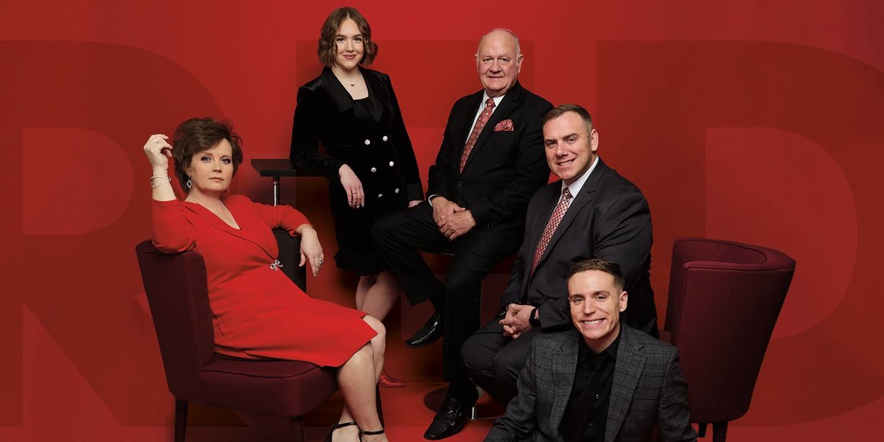 Group of five well-dressed people posing in red-themed setting.