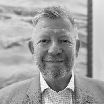 Smiling middle-aged man with a beard in a suit jacket and checkered shirt.