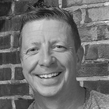 Smiling man with short hair in front of a brick wall.