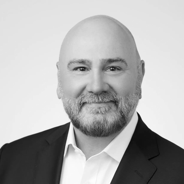 Professional black-and-white portrait of a smiling bald man with a beard in a suit.