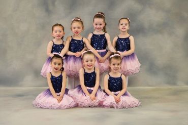 Seven young girls in matching dance costumes posing.