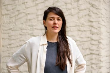 Woman with long brown hair standing against a textured wall.