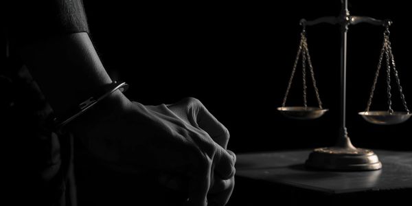 Handcuffed hands in front of a justice scale symbolizing law and order.