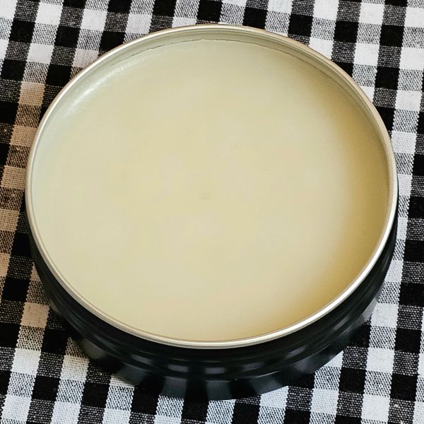 Open tin of smooth, creamy balm on checkered cloth.