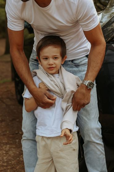 A man helping a young boy wear a sweater outdoors.