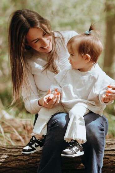 A joyful mother holds her toddler on her lap outdoors, sharing a loving moment.