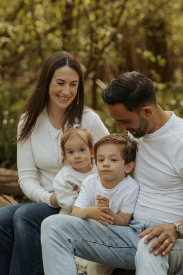 A happy family of four sitting outdoors in casual white tops.