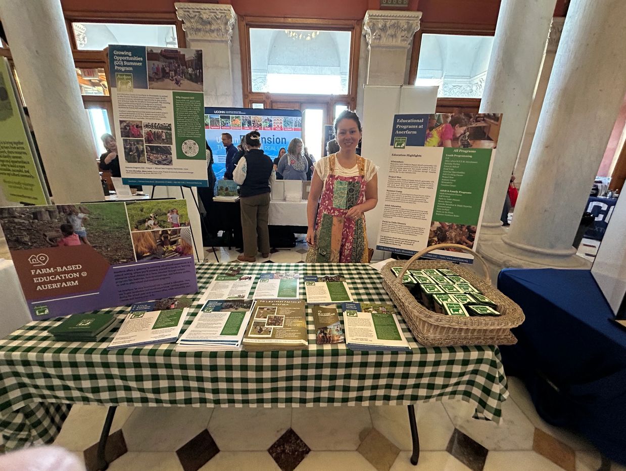 Woman standing behind educational booth with brochures and posters on farm-based education.