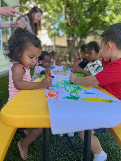 Children painting together outdoors on a sunny day.