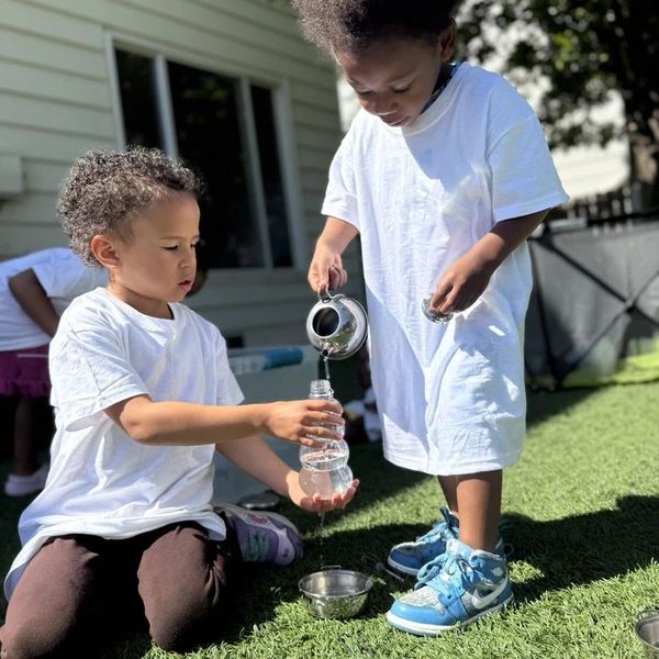 Two kids playing with water outside on grass.