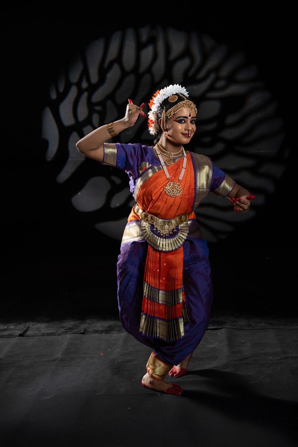 Classical Indian dancer in vibrant traditional attire performing against a dramatic backdrop.