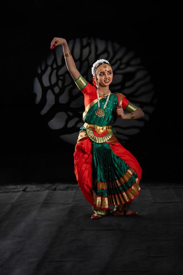 A classical Indian dancer in traditional attire performing against a dark backdrop.
