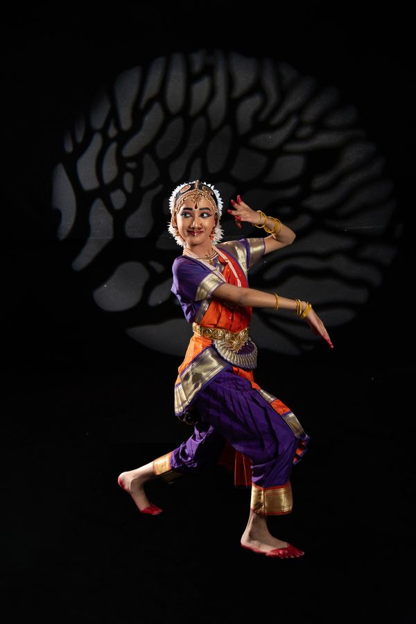 Classical Indian dancer in vibrant costume performing against a tree shadow backdrop.