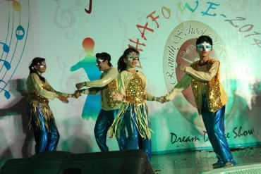 Four dancers in gold and blue costumes performing on stage.