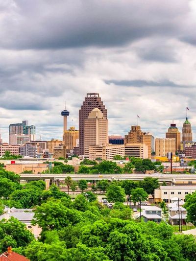Skyline of a city with cloudy skies and lush greenery in the foreground.