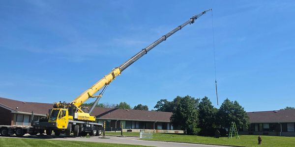 A yellow mobile crane extends its arm high against a blue sky near buildings.