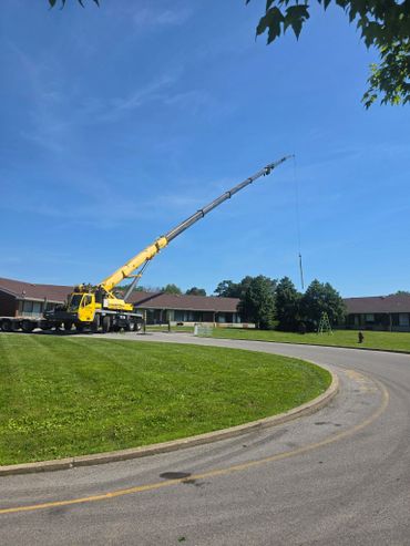 A yellow crane parked on a curved road with houses and trees in the background.