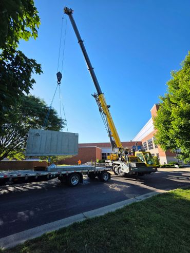 A crane lifts a large concrete slab near a building on a sunny day.