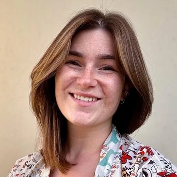 Smiling young woman with shoulder-length brown hair and a patterned shirt.