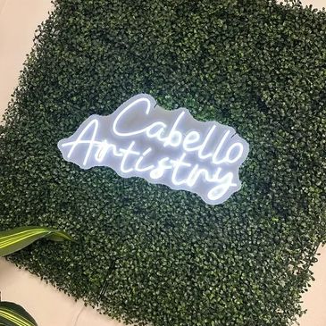 Neon sign "Cabello Artistry" on a green leafy wall.