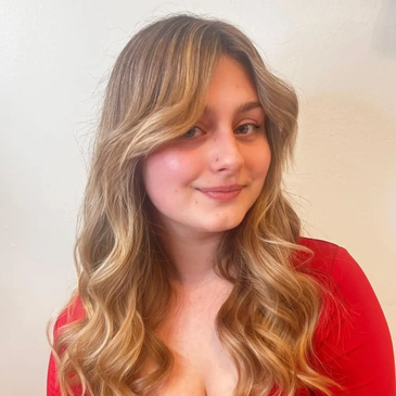 Young woman with long wavy blonde hair and a red top smiling gently.